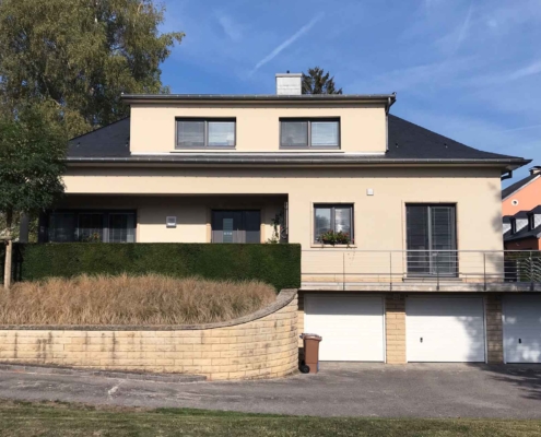 Beiges Einfamilienhaus mit grauen Coplaning PVC Alu-Fenster und einer grauen modernen Coplaning Haustür mit Seitenlicht aus Glas.