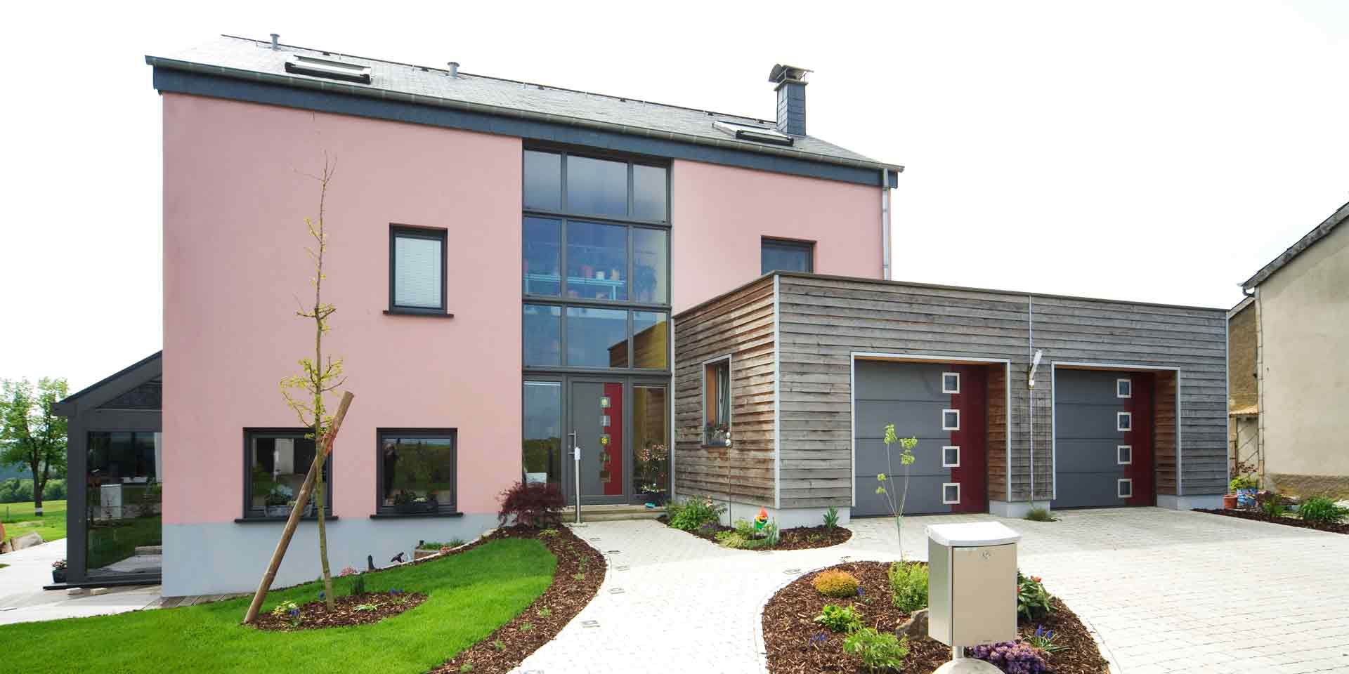 Pinkes Einfamilienhaus in Nocher mit einer rot- grauen Coplaning Haustür, grauen Coplaning Alu Fenster und zwei rot- grauen Coplaning Alu Garagentoren.