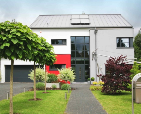 Rot- grau- weißes Einfamilienhaus mit moderner grauer Coplaning Haustür, grauen Coplaning Alu Fenster und einem grauen Coplaning Garagentor.