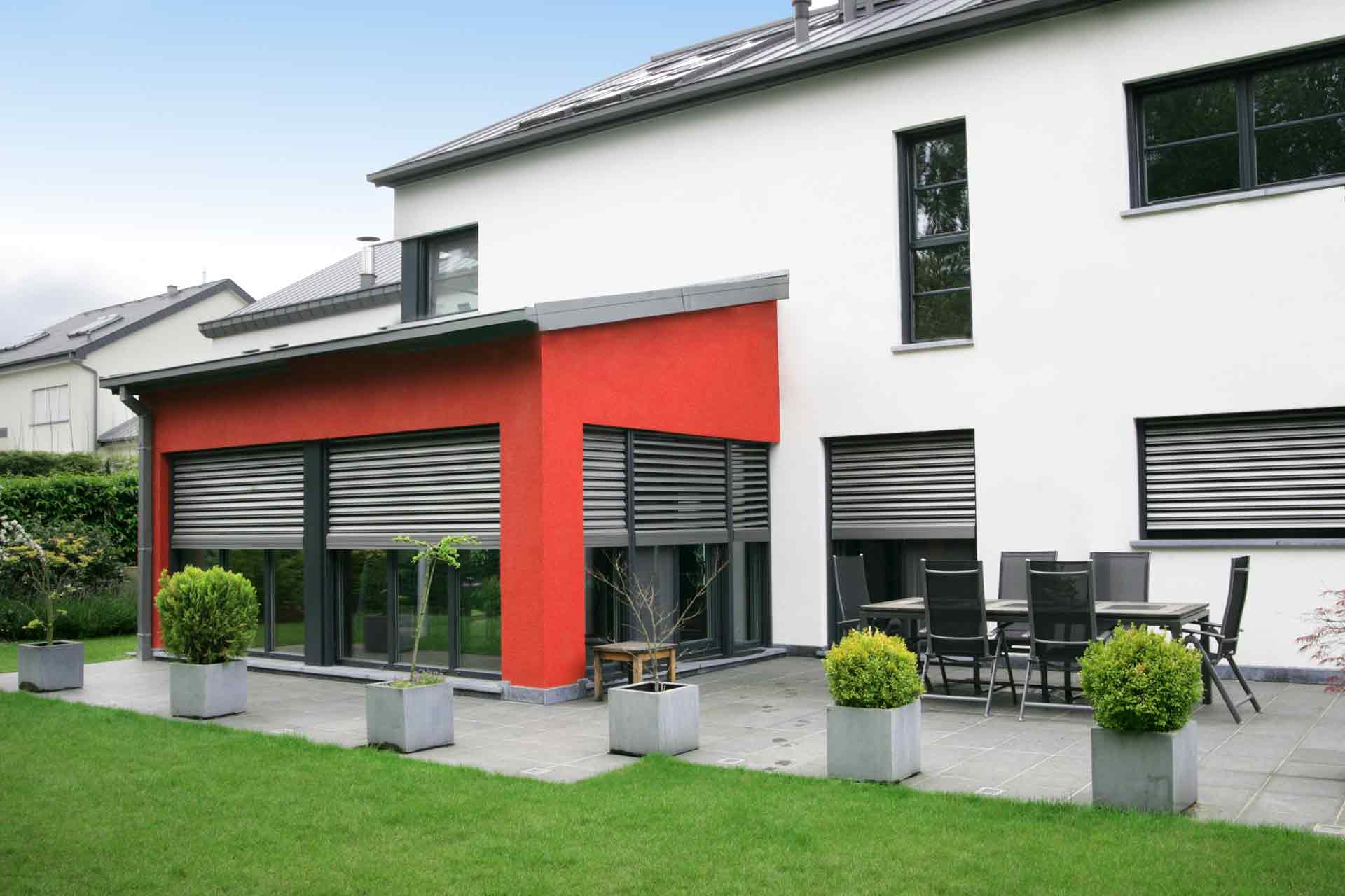 Rückseite des rot- grau- weißen Einfamilienhauses mit Blick auf die grauen Coplaning Alu Fenster.