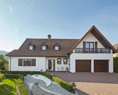 Großes weißes Einfamilienhaus mit einer modernen braun-weißen Coplaning Haustür und braunen Coplaning Holz-Alu Fenster mit integrierten Jalousien