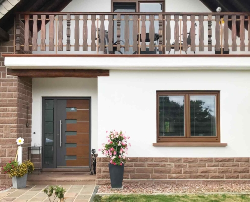 Weiß- braunes Einfamilienhaus mit braun-grauer Coplaning Haustür und Holz Alu Coplaning Fenstern.