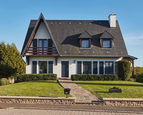 Weißes Einfamilienhaus mit einer grauen Coplaning Alu Haustür und grauen Coplaning Holz- Alu PVC Fenster mit passenden Klappläden.