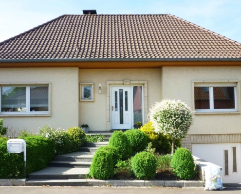 Gelbliches Einfamilienhaus mit einer weißen Coplaning Lack Haustür mit Glas und einem weißen Coplaning Garagentor mit Glausausschnitten.