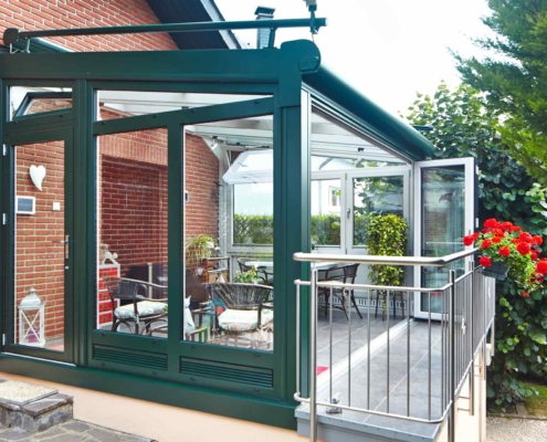 Einfamilienhaus mit Steinfassade mit Nahaufnahme der Rückseite mit Blick auf ein grüner Coplaning Alu Veranda Wintergarten mit weißer geöffneten Faltanlage und Kippfenster.